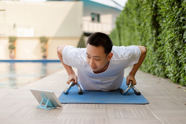 Concepto de gimnasio de entrenamiento un joven adulto haciendo ejercicio mientras navega por las redes sociales con su computadora portátil durante una pandemia de covid-19.