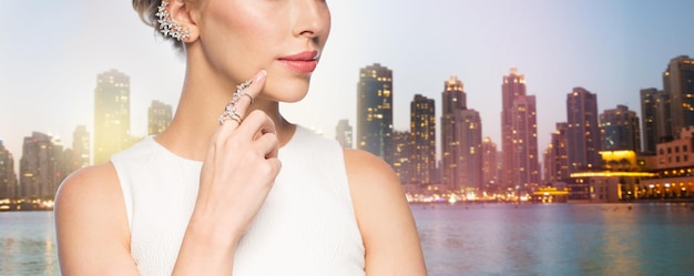 concepto de glamour, belleza, joyería y lujo - cerca de una mujer hermosa con un anillo de oro y un pendiente de diamantes sobre el fondo de los rascacielos de la ciudad de Singapur