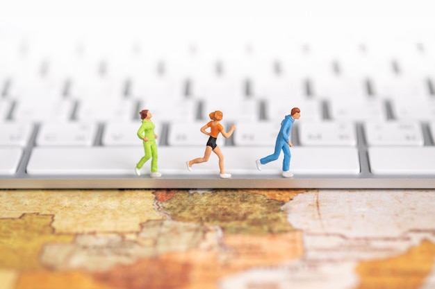 Foto concepto global de deporte y tecnología. cerca del grupo de figuras en miniatura corredor corriendo en el teclado de la computadora en el mapa mundial.