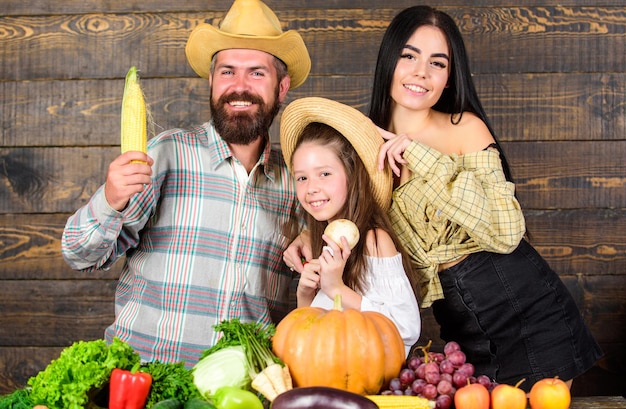 Concepto de granja familiar. Agricultores familiares con fondo de madera de cosecha. Los padres y la hija celebran el festival de la cosecha de otoño. Agricultores familiares de estilo rústico en el mercado con verduras, frutas y vegetación.