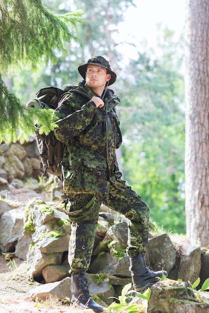 concepto de guerra, caminatas, ejército y personas - joven soldado o guardabosques con mochila caminando en el bosque