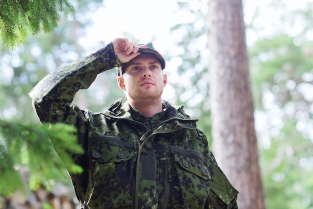 concepto de guerra, ejército y gente - joven soldado o guardabosques con uniforme militar en el bosque