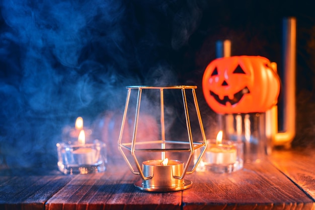 Concepto de Halloween decoraciones espeluznantes con velas encendidas y portavelas con humo de tono azul alrededor de una mesa de madera oscura de cerca