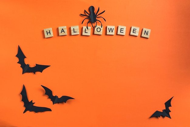 Concepto de Halloween y decoraciones de papel. La inscripción de cubos de madera y murciélagos cortados de papel negro sobre un fondo naranja. Estilo de corte de papel. Espacio de copia de vista superior