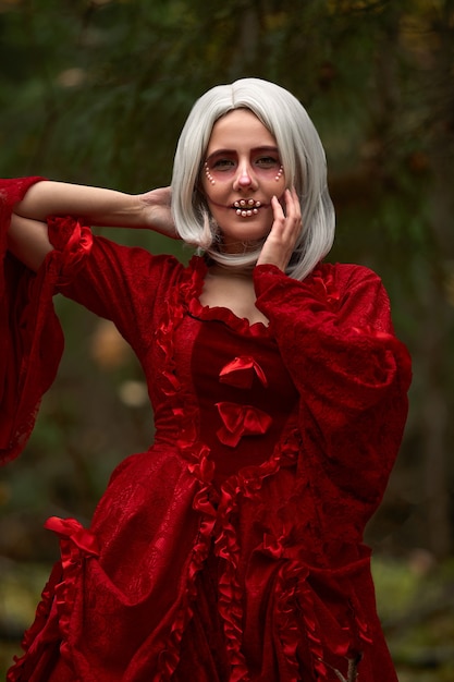 Concepto de Halloween, detalle de traje glamoroso. Joven mujer hermosa y misteriosa en el bosque, con vestido blanco y capa roja. Caperucita roja o cuento de vampiros.