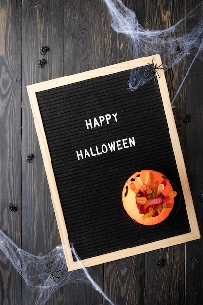 Concepto de Halloween. Dulces de fiesta de Halloween con tablero de letras negro con palabras Feliz Halloween plana yacía sobre fondo de madera negra con tela de araña