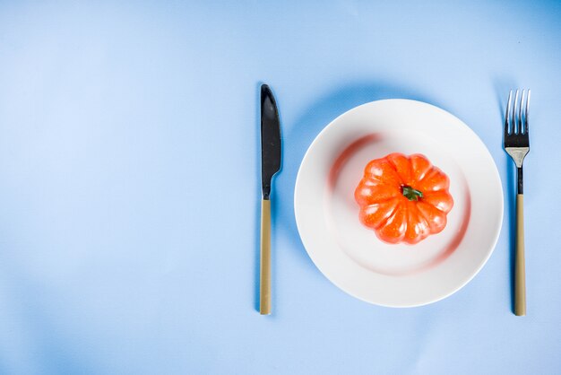 Concepto de Halloween, fondo comedor con plato, tenedor, cuchillo y calabaza decorativa, espacio de copia de fondo azul claro arriba