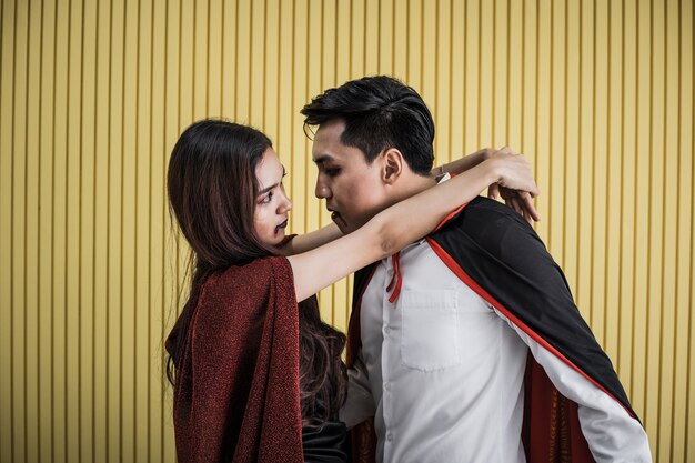 Concepto de Halloween de joven asiática en traje de bruja y hombre asiático en traje de Drácula sobre fondo amarillo. Retrato de pareja de adolescentes disfrazados de brujas y Drácula para celebrar el festival de Halloween.