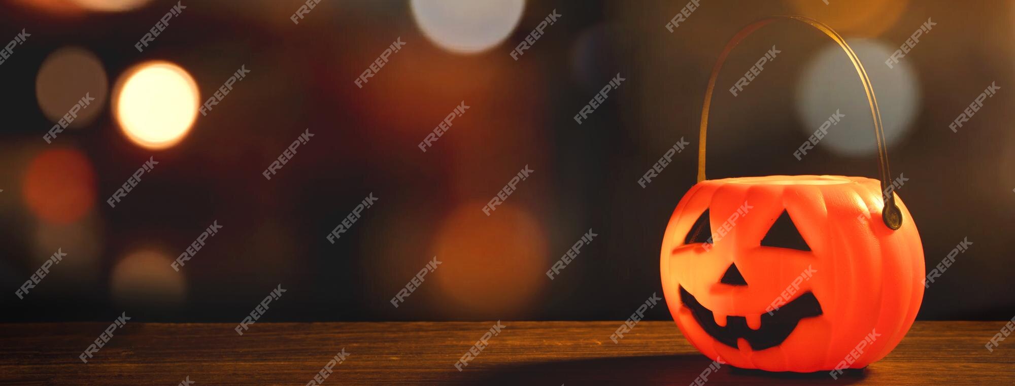 Concepto de halloween linterna de calabaza de plástico naranja sobre una mesa de madera oscura con luz brillante borrosa en el fondo truco o trato de cerca | Foto Premium Concepto de halloween linterna de calabaza de plástico naranja sobre una mesa de madera oscura con luz brillante borrosa en el fondo truco o trato de cerca | Foto Premium
