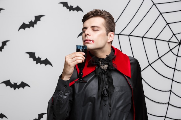 Concepto de Halloween vampiro - retrato de vampiro caucásico guapo disfrutar bebiendo vino tinto con sangre.