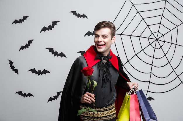 Concepto de Halloween del vampiro - Vampiro caucásico hermoso feliz que sostiene el bolso de compras colorido.