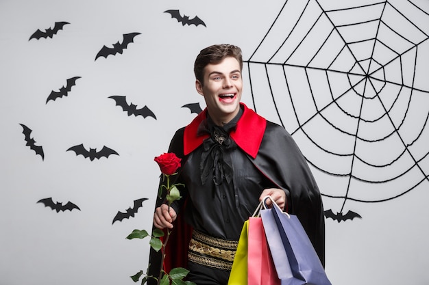 Concepto de Halloween del vampiro - Vampiro caucásico hermoso feliz que sostiene el bolso de compras colorido.