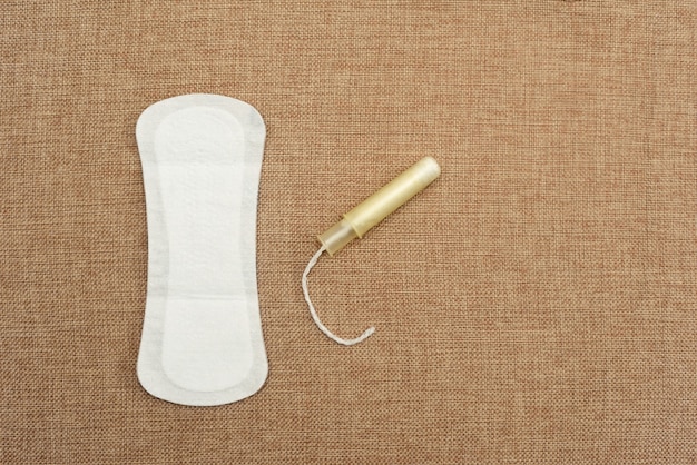 Concepto de higiene femenina con toalla sanitaria y tampón sobre una base de tejido natural