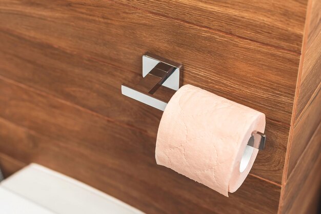 Concepto de higiene Rollo de papel higiénico rosa sobre soporte de papel metálico en el interior de un hermoso concepto sanitario de baño marrón oscuro de madera