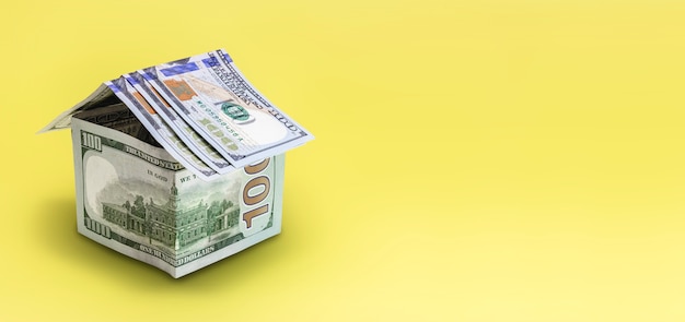 El concepto de hipoteca y alquiler de viviendas e inmuebles. Préstamos de crédito hipotecario. Casa hecha de billetes de un dólar sobre un fondo amarillo.
