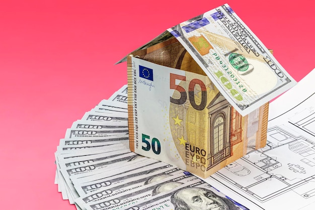 El concepto de hipoteca y vivienda de alquiler y bienes raíces Préstamo de crédito hipotecario Casa de billetes en euros en el plano de la casa y billetes en dólares dispuestos sobre un fondo azul