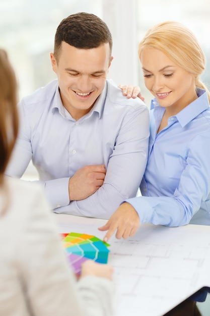 Foto concepto de hogar, diseño y arquitectura - pareja sonriente mirando muestras de planos y colores en la oficina