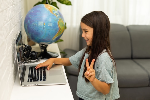 concepto de hogar, ocio, tecnología e internet - niña estudiante con computadora portátil en casa, niña usa video chat