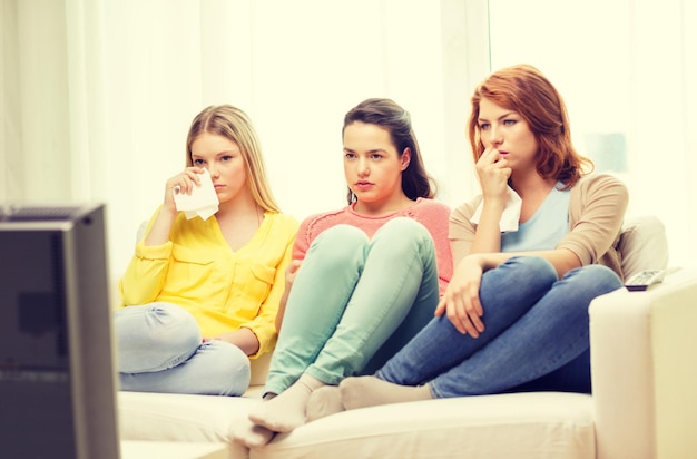 concepto de hogar, tecnología y amistad - tres adolescentes tristes viendo la televisión en casa