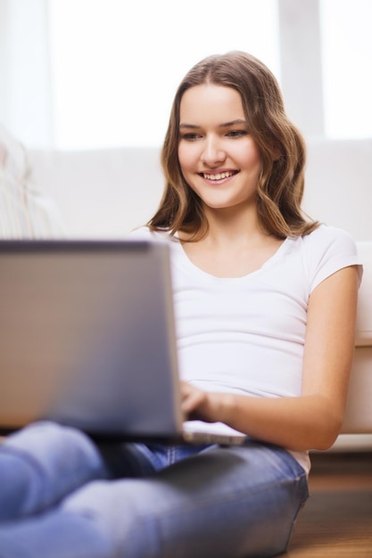 concepto de hogar, tecnología e Internet - adolescente sonriente sentada en el suelo con una computadora portátil en casa