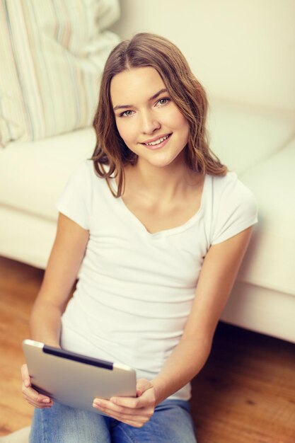 concepto de hogar, tecnología e Internet - adolescente sonriente sentada en el suelo con una tableta en casa