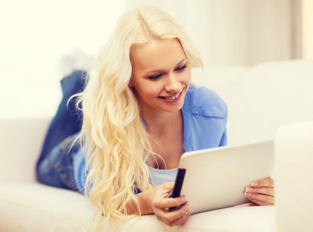 concepto de hogar, tecnología e Internet - mujer sonriente tendida en el sofá con una computadora de tablet pc en casa