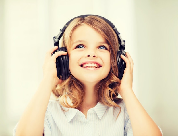 concepto de hogar, tecnología y música - niña pequeña con auriculares en casa