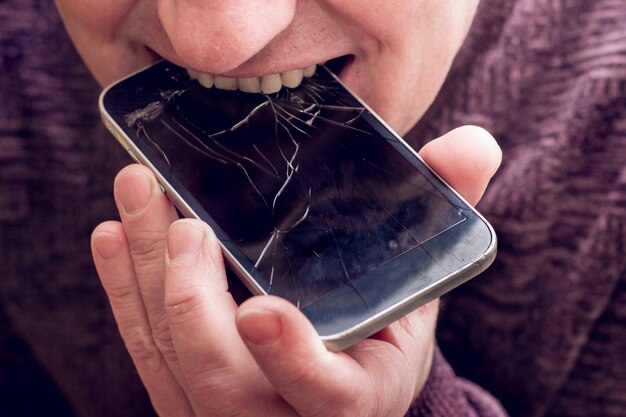 Concepto de hombre mordiendo un teléfono roto