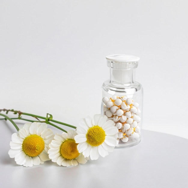 Foto concepto homeopático camomila en un frasco transparente y granos homeopáticos sobre un fondo blanco