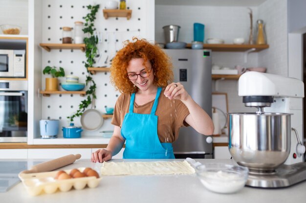 Concepto de horneado Retrato de una mujer alegre kneading masa en el interior de la cocina mujer alegre en delantal divirtiéndose mientras prepara pasteles caseros