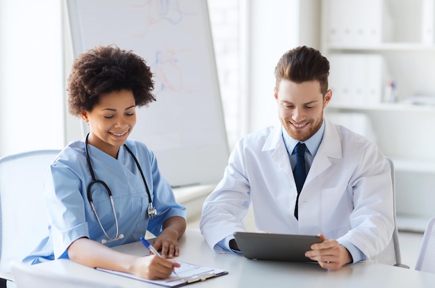 concepto de hospital, profesión, personas y medicina - dos médicos felices con una reunión de computadora de tablet pc y hablando en el consultorio médico