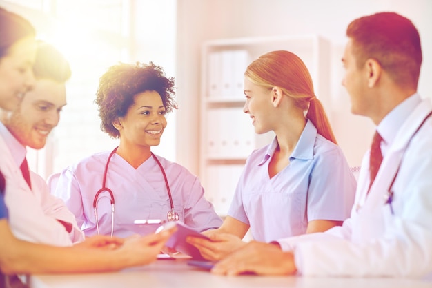 concepto de hospital, profesión, personas y medicina - grupo de médicos felices con computadoras tabletas que se reúnen en la oficina médica