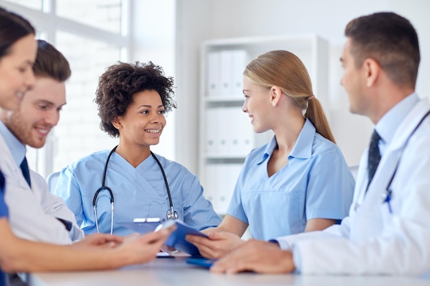 concepto de hospital, profesión, personas y medicina - grupo de médicos felices con tabletas reunidas en el consultorio médico