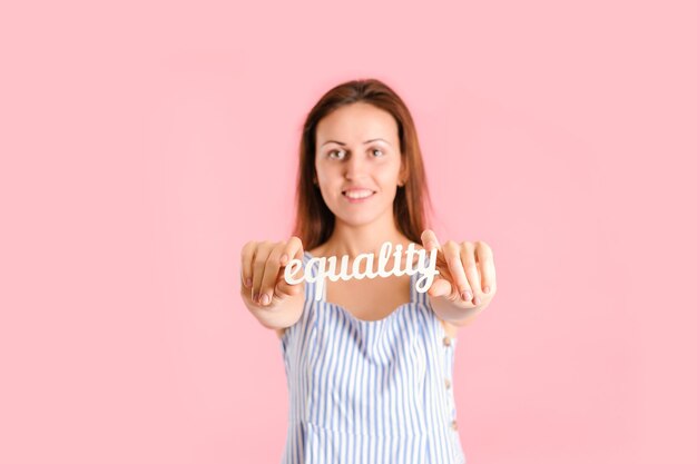 El concepto de igualdad de género. Una mujer sobre un fondo rosa con la palabra IGUALDAD en la mano. Foto de estudio sobre un fondo rosa