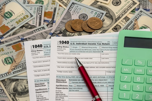 Concepto de impuestos y contabilidad, calculadora de pluma de formulario 1040 y billetes de dólar