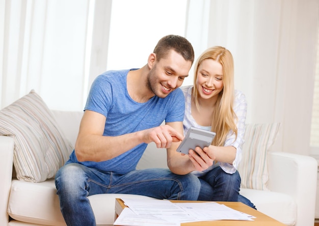 concepto de impuestos, finanzas, familia, hogar y felicidad - pareja sonriente con papeles y calculadora en casa