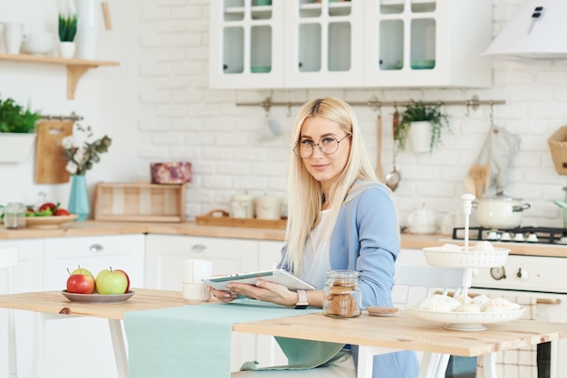 Concepto independiente. hermosa mujer de negocios en ropa casual y gafas está examinando documentos y sonriendo mientras trabajaba con una computadora portátil en la cocina