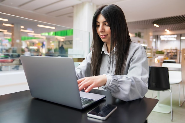 Concepto independiente Una mujer está escribiendo en una computadora portátil mientras está sentada en un café del centro comercial