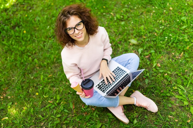 Concepto independiente. niña sentada en el césped con laptop y café