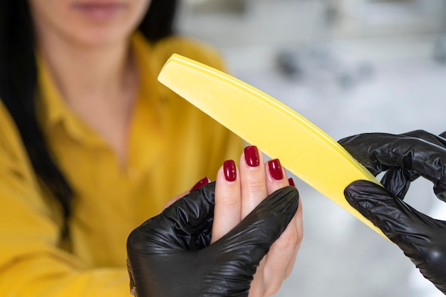 Concepto de la industria de la belleza Mujer manicurista maestra con guantes está pulindo las uñas del cliente usando un archivo Retrato de una mujer joven que trabaja en una clínica de salón de cosmetología Higiene y cuidado de las manos