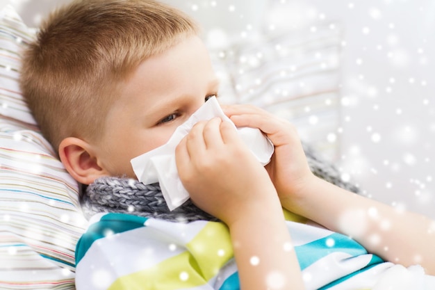 concepto de infancia, atención médica y personas - niño enfermo con gripe soplando la nariz en el tejido en casa