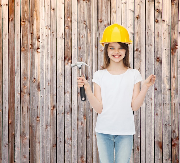 concepto de infancia, construcción, arquitectura, construcción y personas - niña sonriente con casco protector con martillo