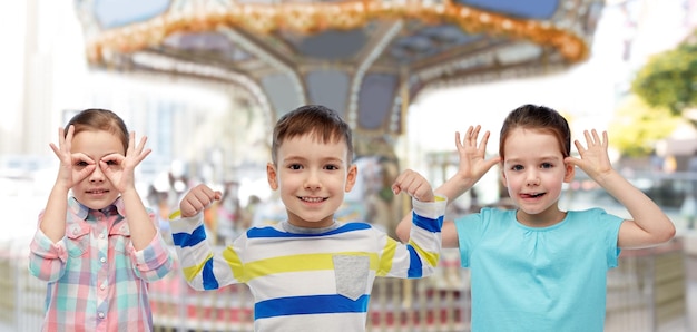 concepto de infancia, entretenimiento y personas - niños pequeños felices divirtiéndose sobre el carrusel y el fondo del parque de atracciones