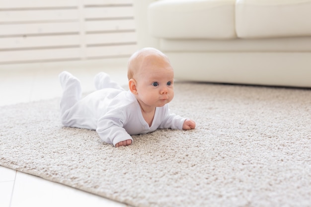 Foto concepto de infancia, infancia y personas: niño o niña gateando por el piso en casa y mirándote.