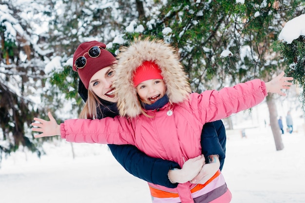 Concepto de infancia, moda, temporada y personas - Niña linda mirando a su madre que está soplando la nieve. Familia feliz durante el invierno caminar al aire libre por la mañana en un clima frío y soleado.