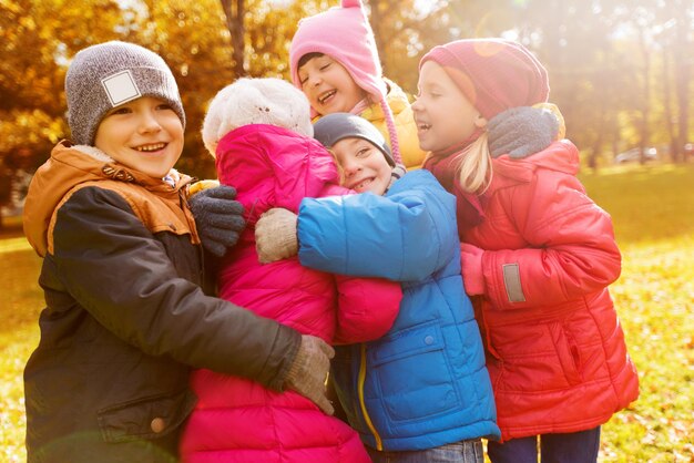 concepto de infancia, ocio, amistad y personas - grupo de niños felices abrazándose en el parque de otoño