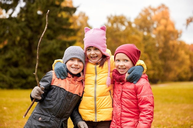 concepto de infancia, ocio, amistad y personas - grupo de niños felices abrazándose en el parque de otoño