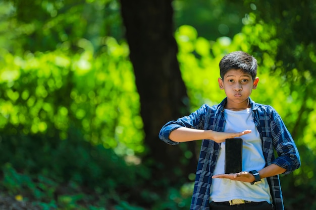 Concepto de infancia, tecnología y personas - niño de escuela lindo indio mostrando teléfono inteligente con pantalla en blanco