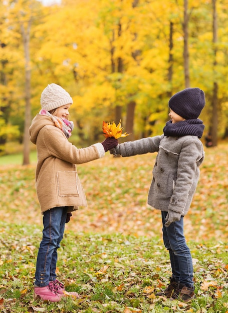 concepto de infancia, temporada y personas - niña y niño sonrientes con hojas de otoño en el parque