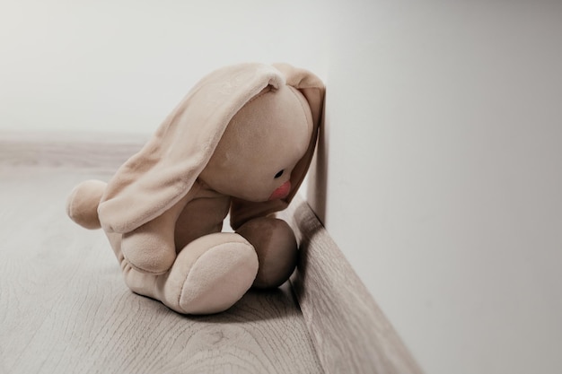 Concepto infantil de tristeza Conejito de juguete sentado apoyado contra la pared de la casa solo el primer plano se ve triste y decepcionado